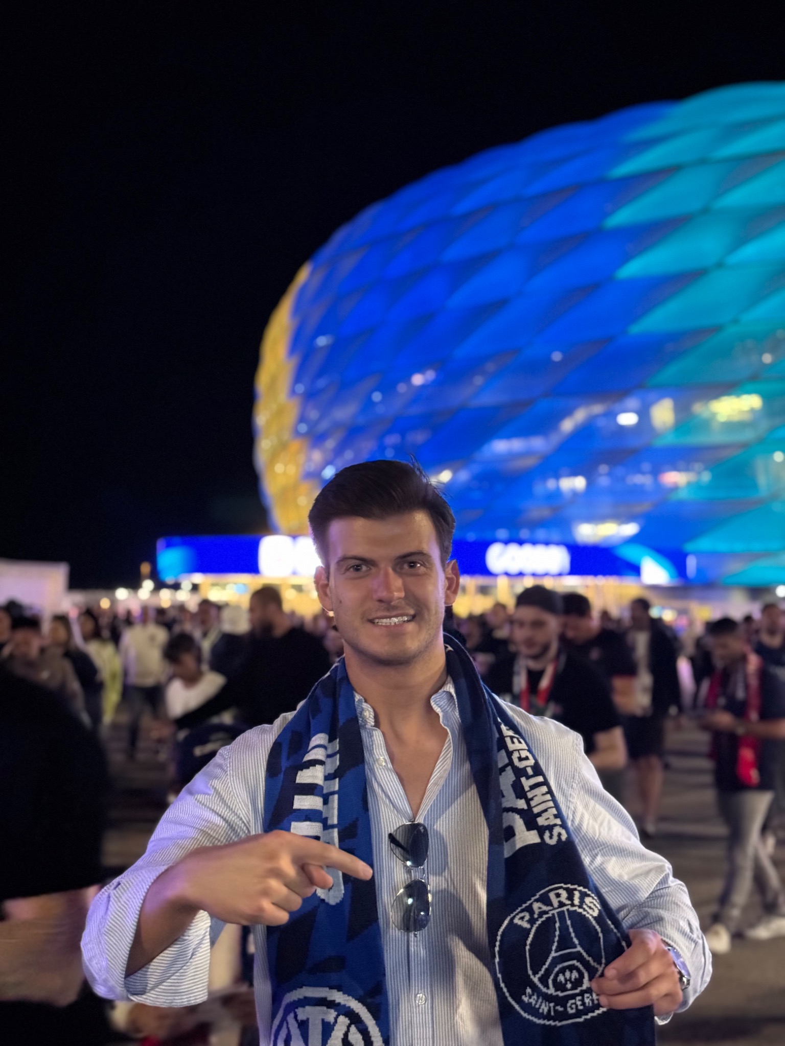Leon in front of a brightly lit football stadium, holding a scarf